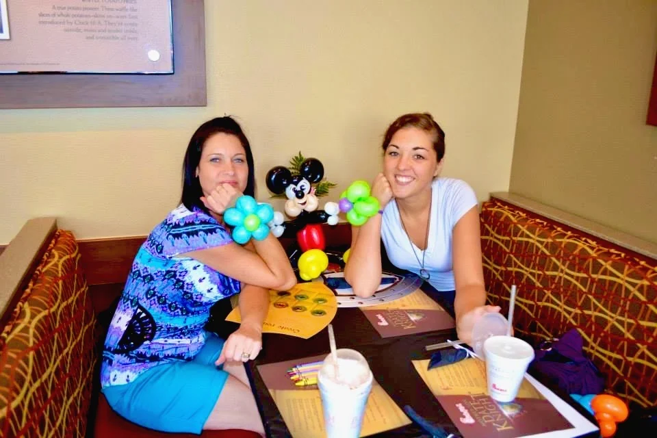 Two adult restaurant guests seated at a table with colorful balloon decorations.