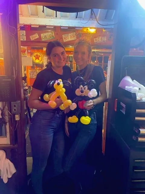 Two adults standing together indoors and holding balloon sculptures.
