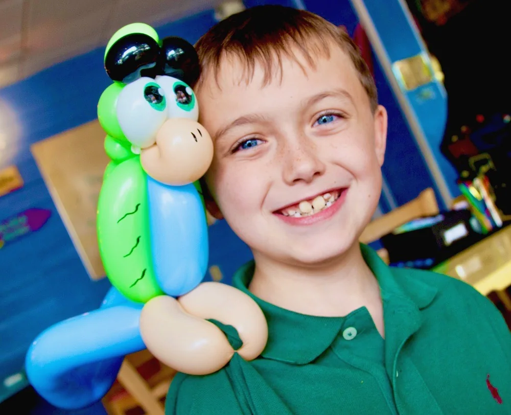 A smiling boy holding a green and blue balloon animal beside his face.
