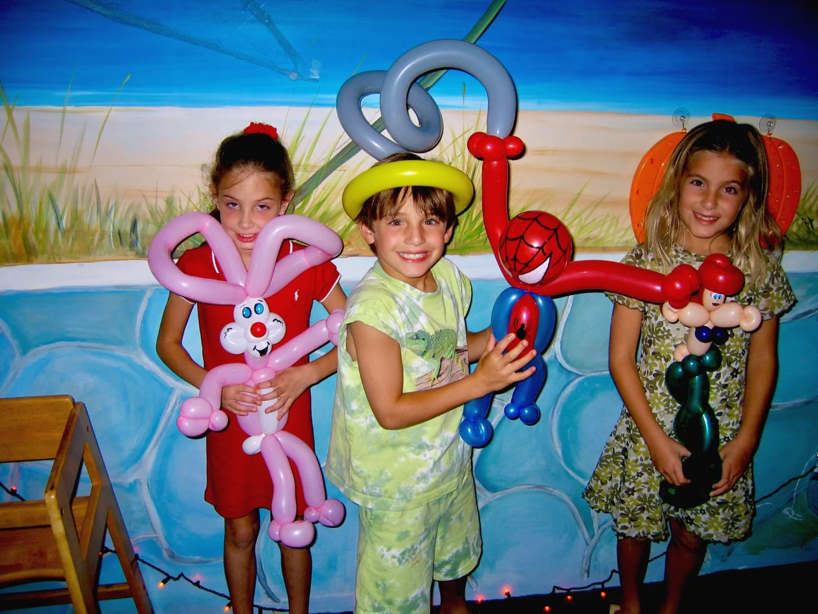 Three children smiling with colorful balloon sculptures during a restaurant kids night.